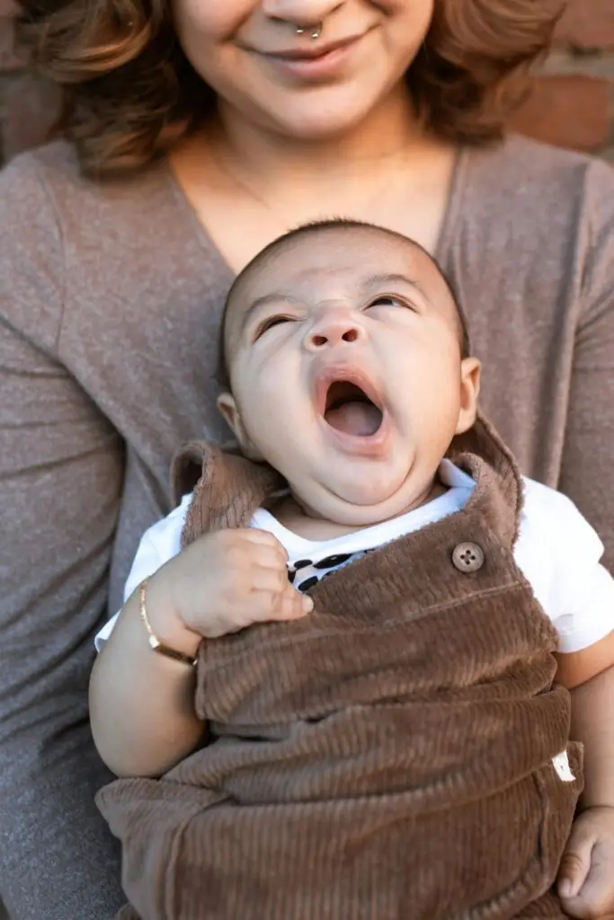 A cute baby yawns while being held, capturing a tender parent-child moment.